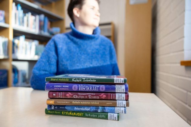 Lukemaan innostaja katselee ikkunasta ulos kirjapinon takana.