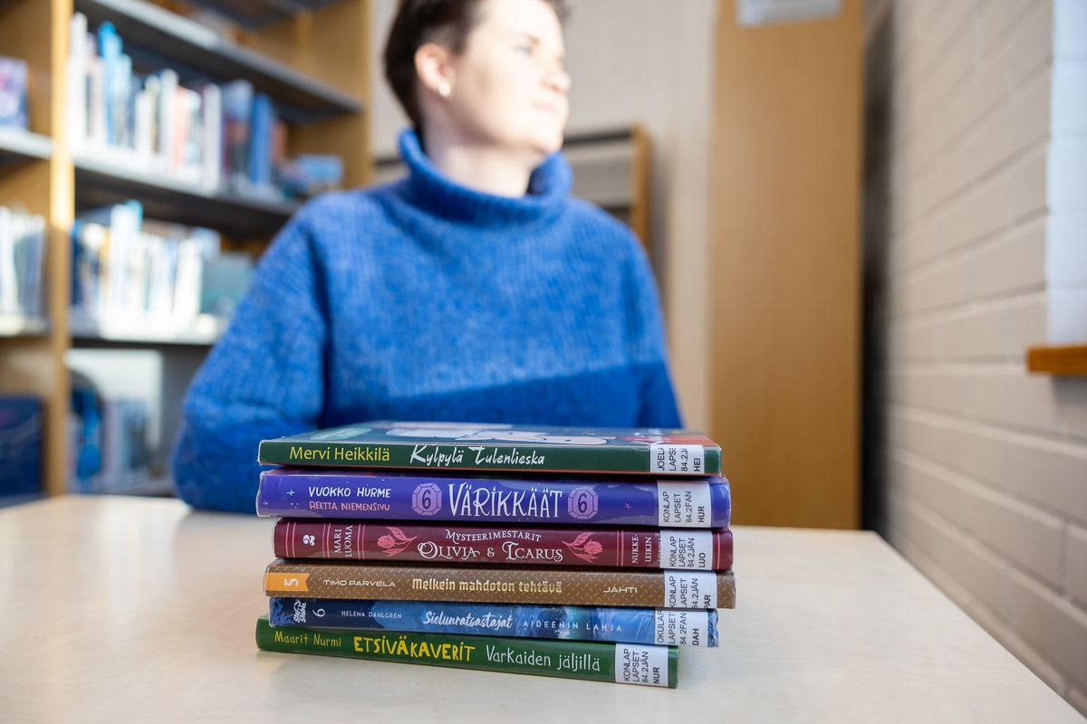 Lukemaan innostaja katselee ikkunasta ulos kirjapinon takana.